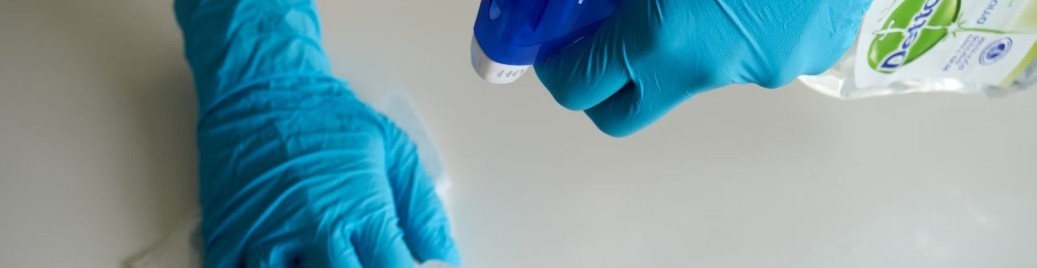 Person med blå handskar rengör yta med papper och sprayflaska